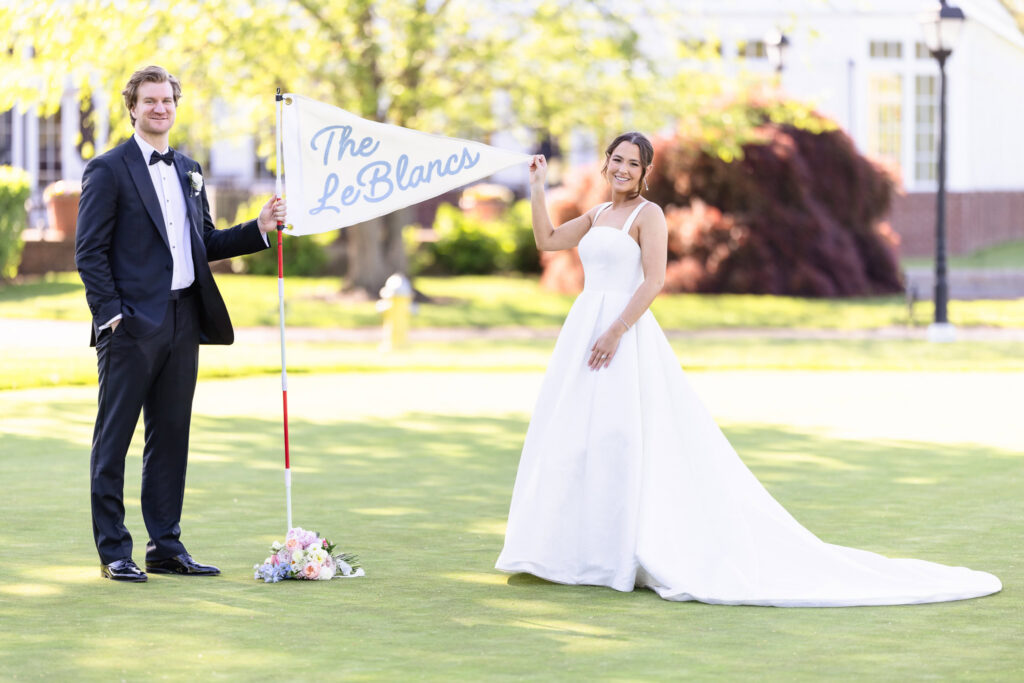 Ashley and Kyle hold a personalized "The LeBlancs" flag on the golf course at The Heritage Club at Bethpage during their wedding portraits.