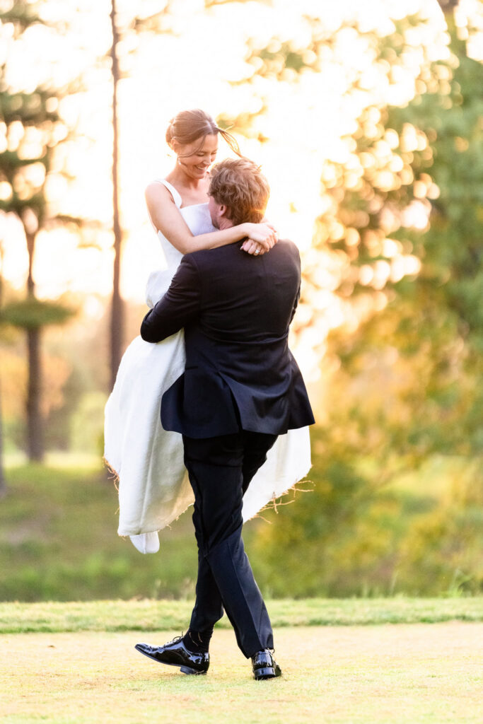 Kyle lifts Ashley during golden hour portraits at The Heritage Club at Bethpage on their wedding day.