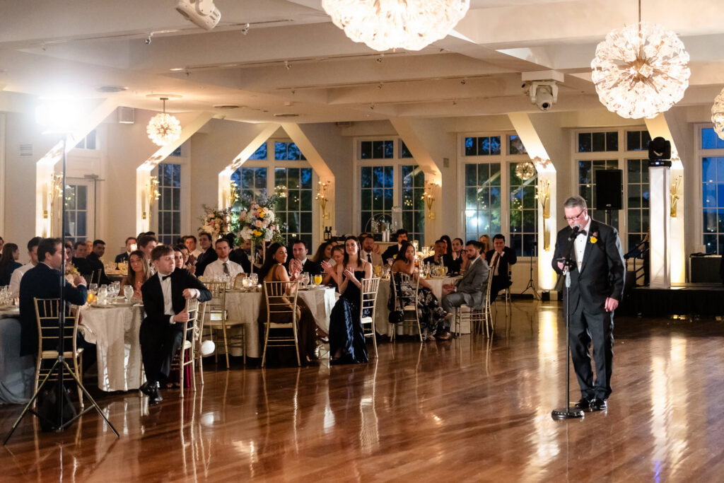 A wedding guest delivers a speech during Ashley and Kyle’s reception at The Heritage Club at Bethpage as guests listen attentively.