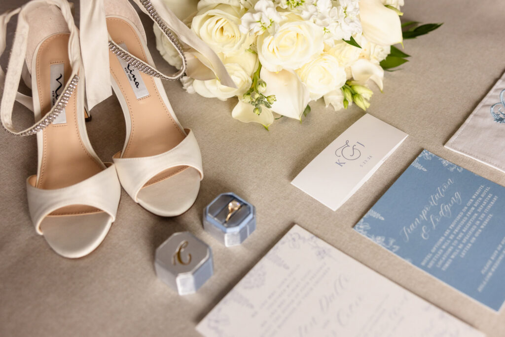 Bridal details featuring ivory heels, white bouquet, invitation suite, and wedding rings.