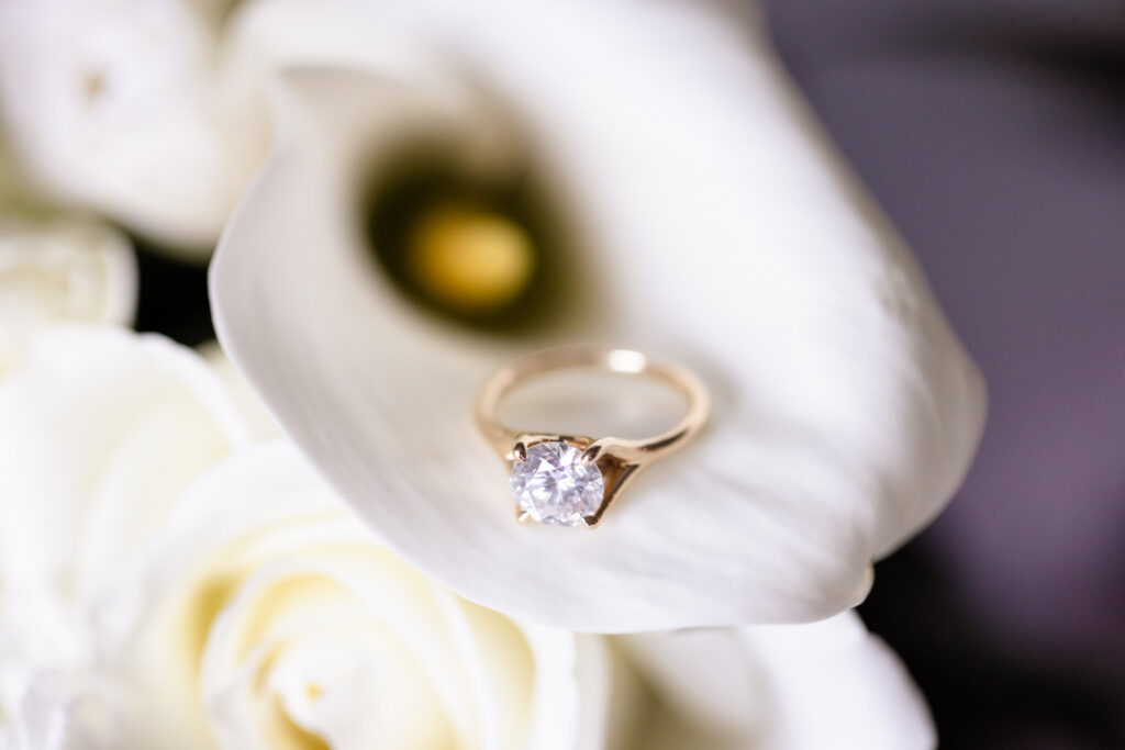 Close-up of a solitaire engagement ring resting on a white calla lily.