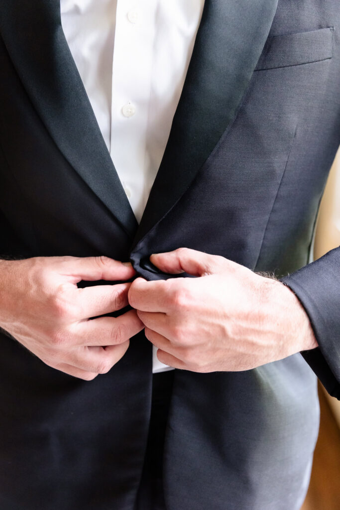 Groom buttoning his black tuxedo jacket while getting ready for a Huntington Crescent Club wedding.