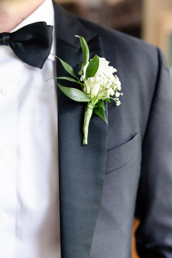 Classic white rose boutonniere pinned to the groom's tuxedo before a Huntington Crescent Club wedding.