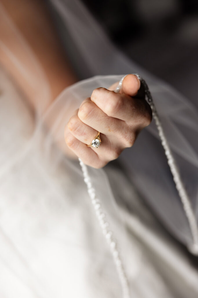Close-up portrait of the bride's engagement ring framed by her wedding veil before a Huntington Crescent Club wedding.