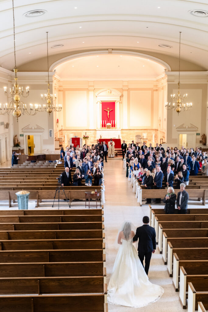 Bride walking down the church aisle with her escort during the ceremony.