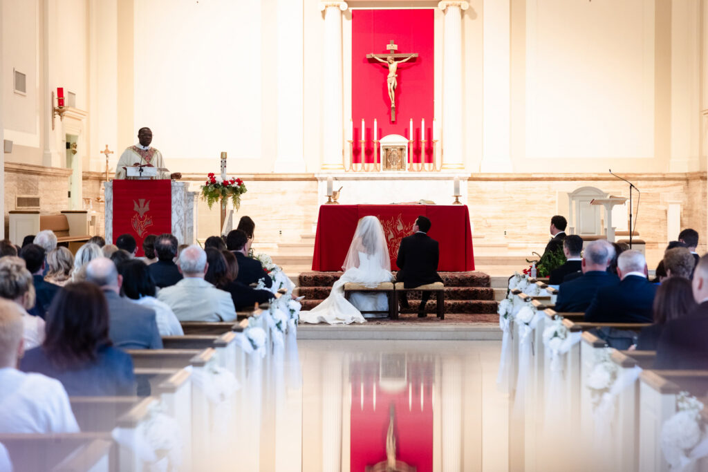 Bride and groom kneeling during their Catholic wedding ceremony before celebrating at their Huntington Crescent Club wedding reception.