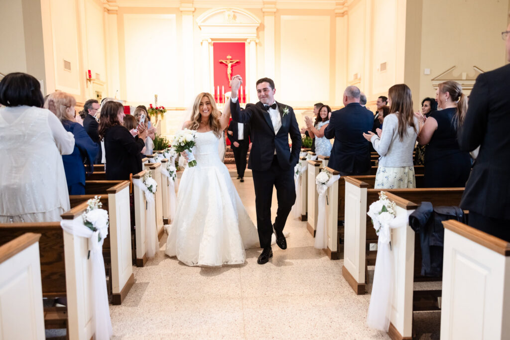 Newly married couple celebrating as they walk down the church aisle following their ceremony before the Huntington Crescent Club wedding reception.