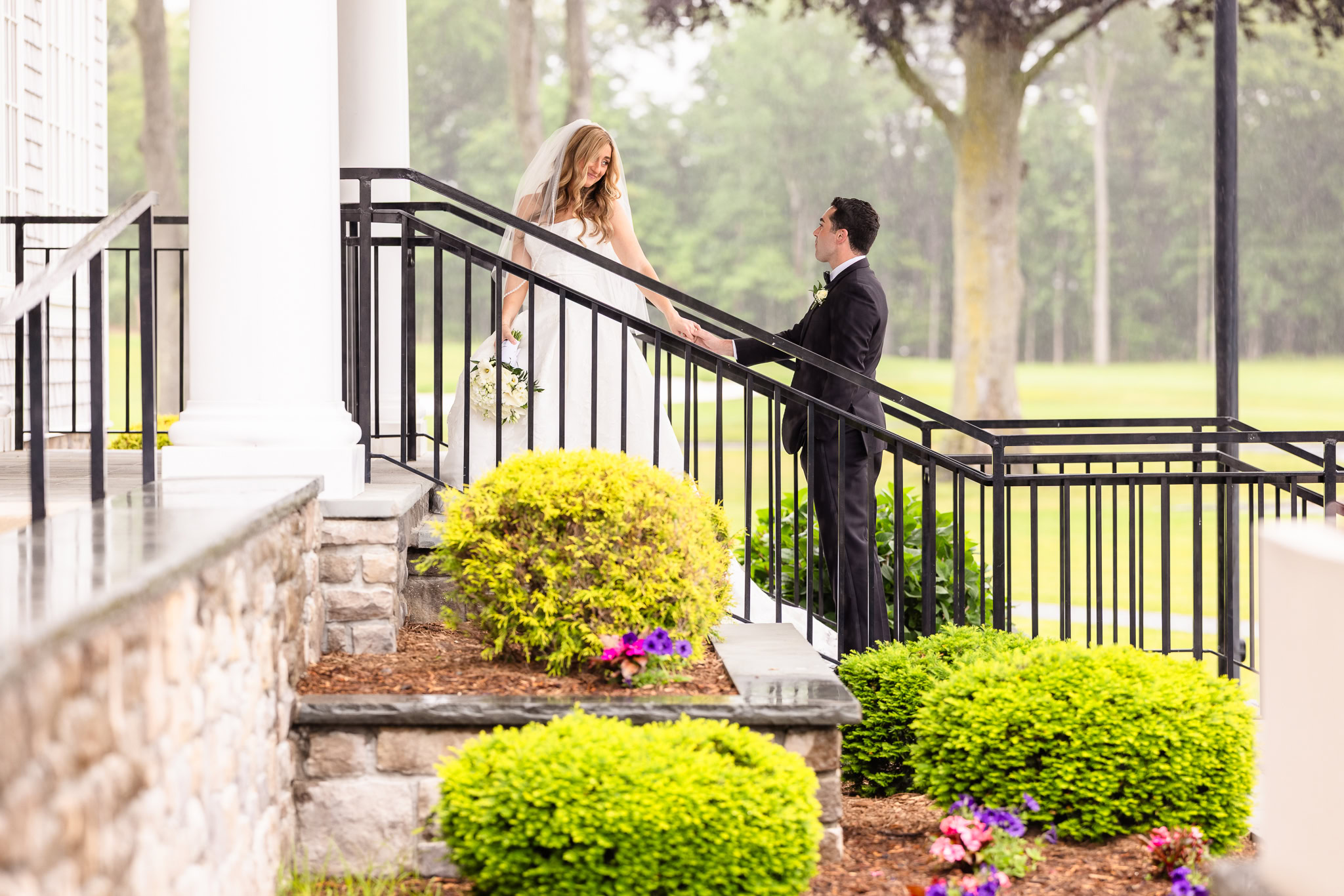Bride and groom holding hands on the covered porch during a rainy Huntington Crescent Club wedding.
