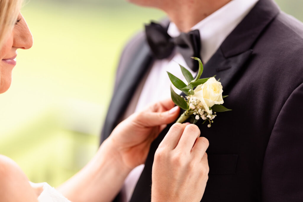 Close-up of the bride adjusting the groom's white rose boutonniere during their Huntington Crescent Club wedding portraits.