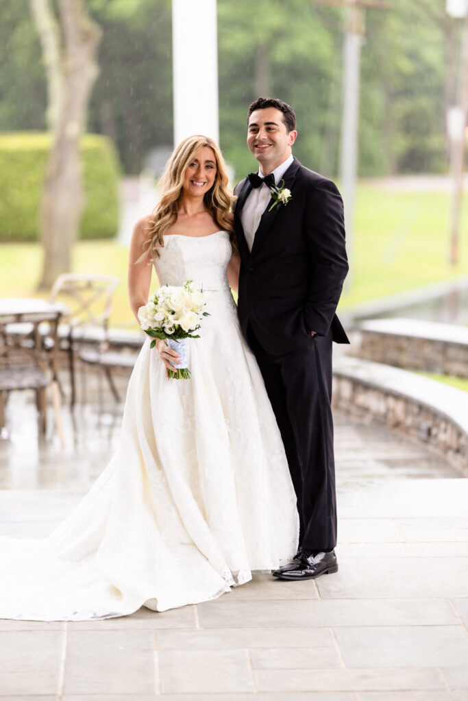 Bride and groom smiling together beneath the covered patio during a rainy Huntington Crescent Club wedding.