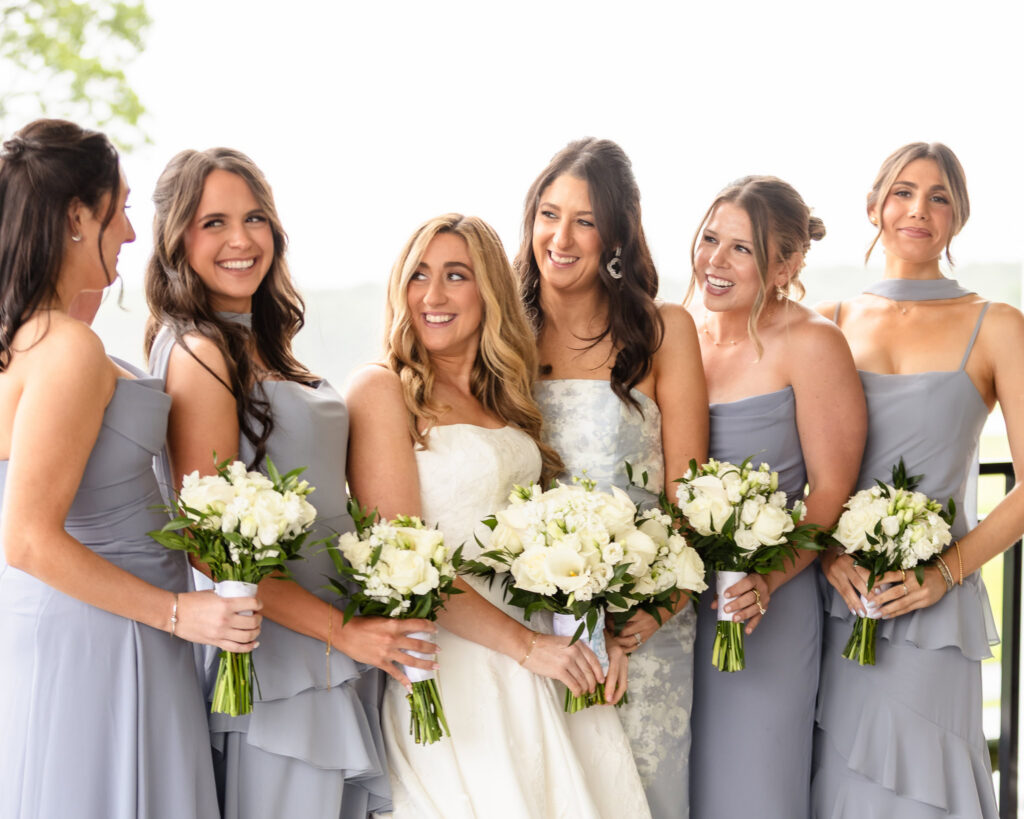 Bride posing with her bridesmaids holding white floral bouquets.