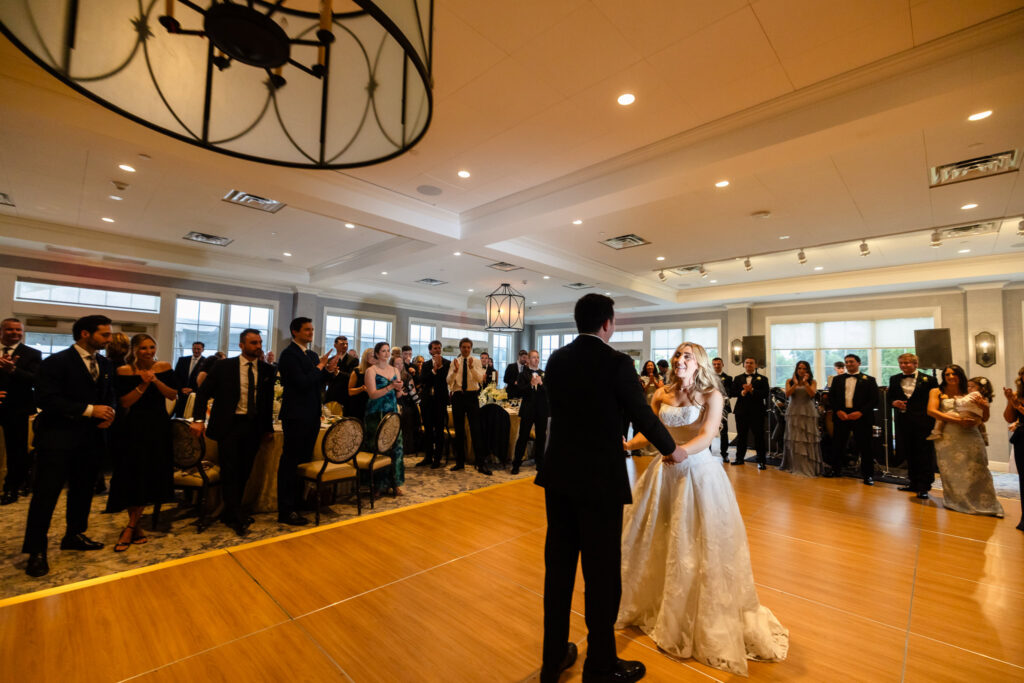 Bride and groom sharing their first dance surrounded by cheering guests at a Huntington Crescent Club wedding.