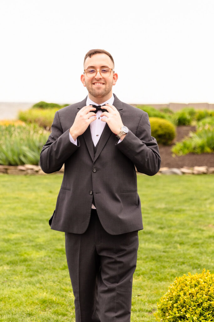 Groom adjusting his bow tie outdoors before a spring wedding at Land's End on the Great South Bay.