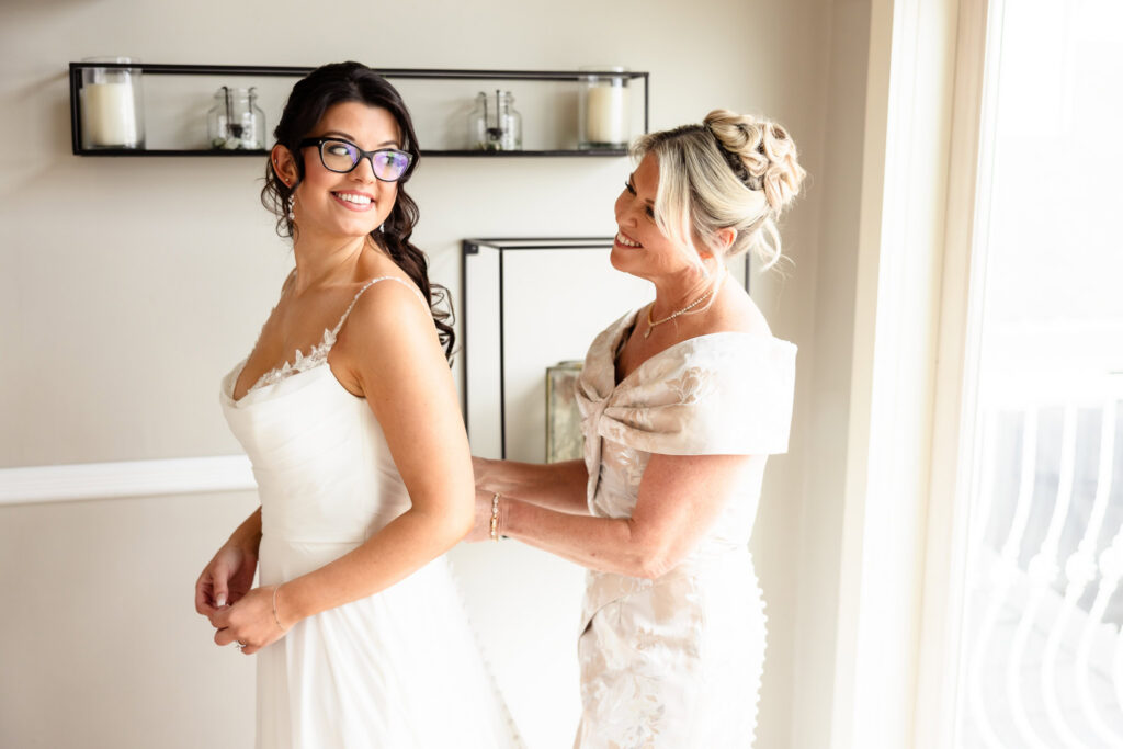 Mother helping the bride into her wedding dress before a spring wedding at Land's End.