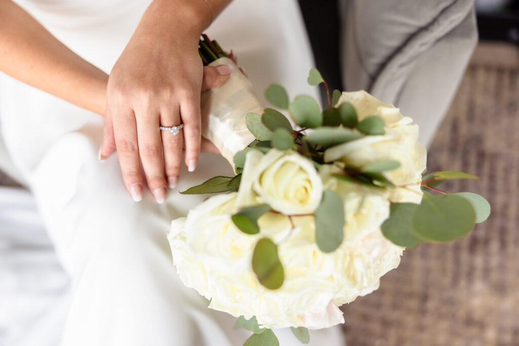 Bride's engagement ring resting on a bouquet of white roses during a spring wedding at Land's End.