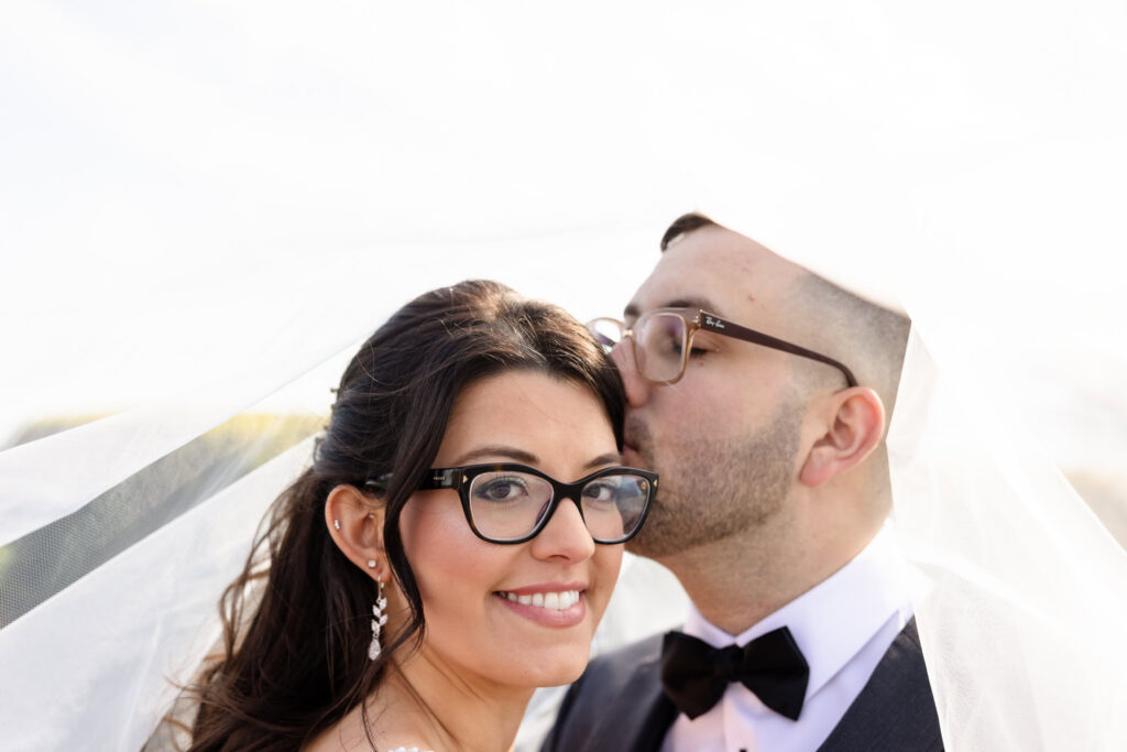Groom kisses his bride beneath her veil.