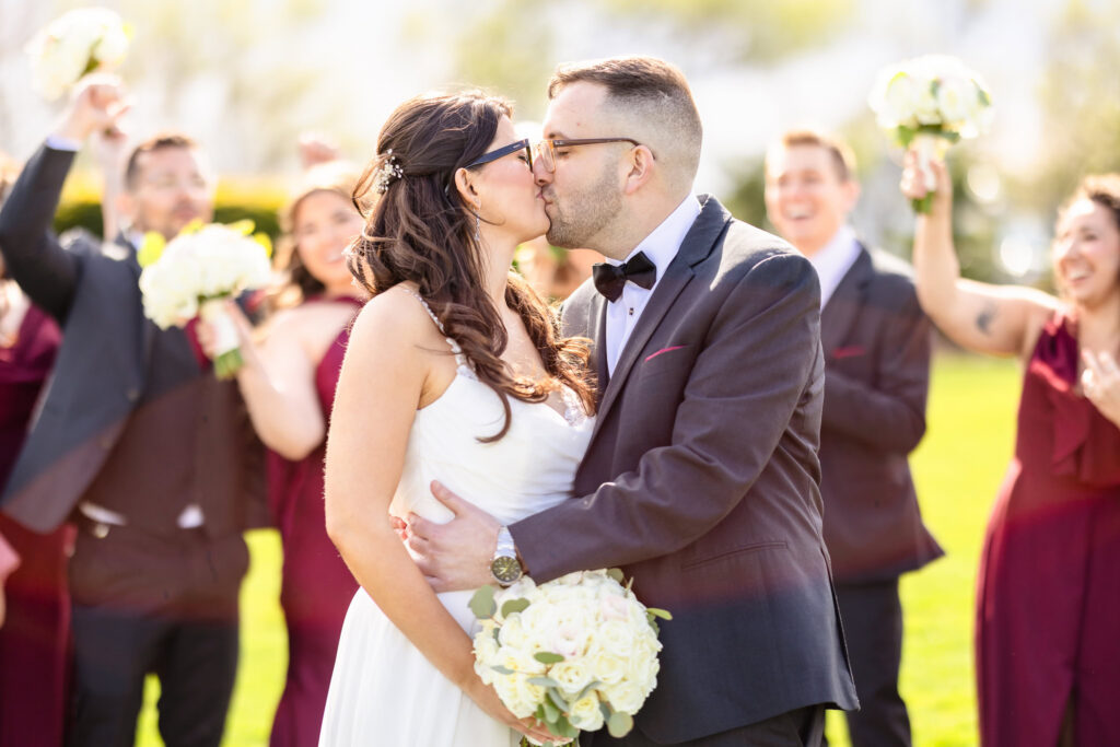 Newlyweds share a kiss surrounded by their cheering wedding party.