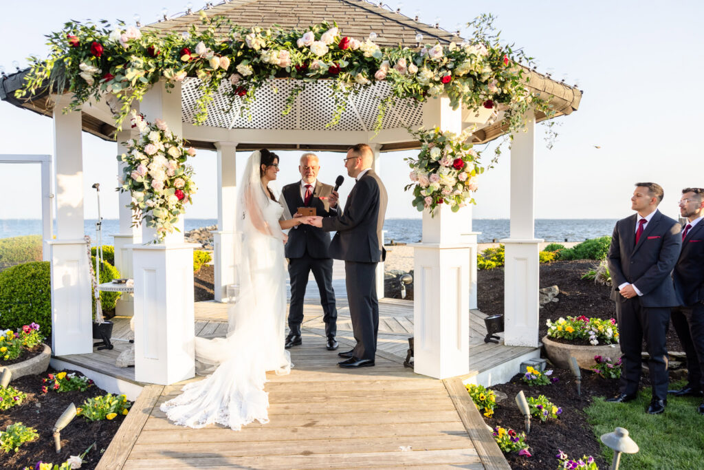 Bride and groom exchanging vows beneath a floral gazebo during a spring wedding at Land's End waterfront ceremony.