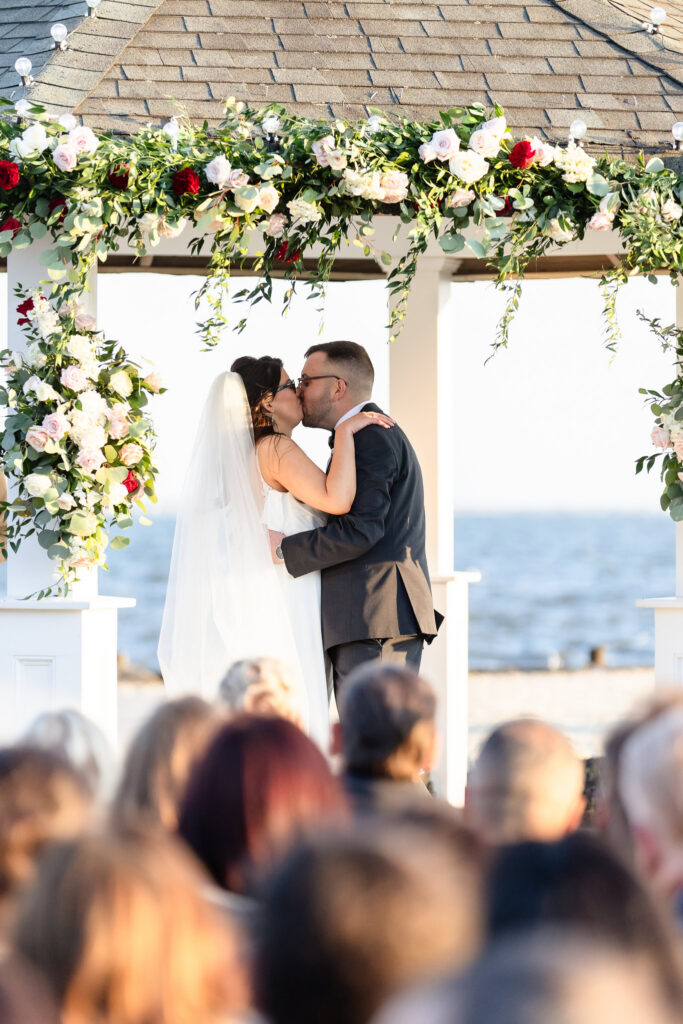 Newlyweds sharing their first kiss beneath a floral arbor during a spring wedding at Land's End.