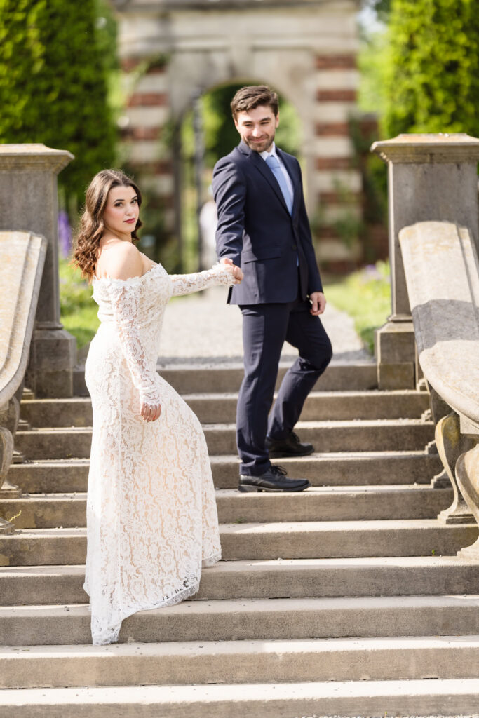 Couple holding hands on the grand stone staircase during an editorial Old Westbury Gardens engagement session.