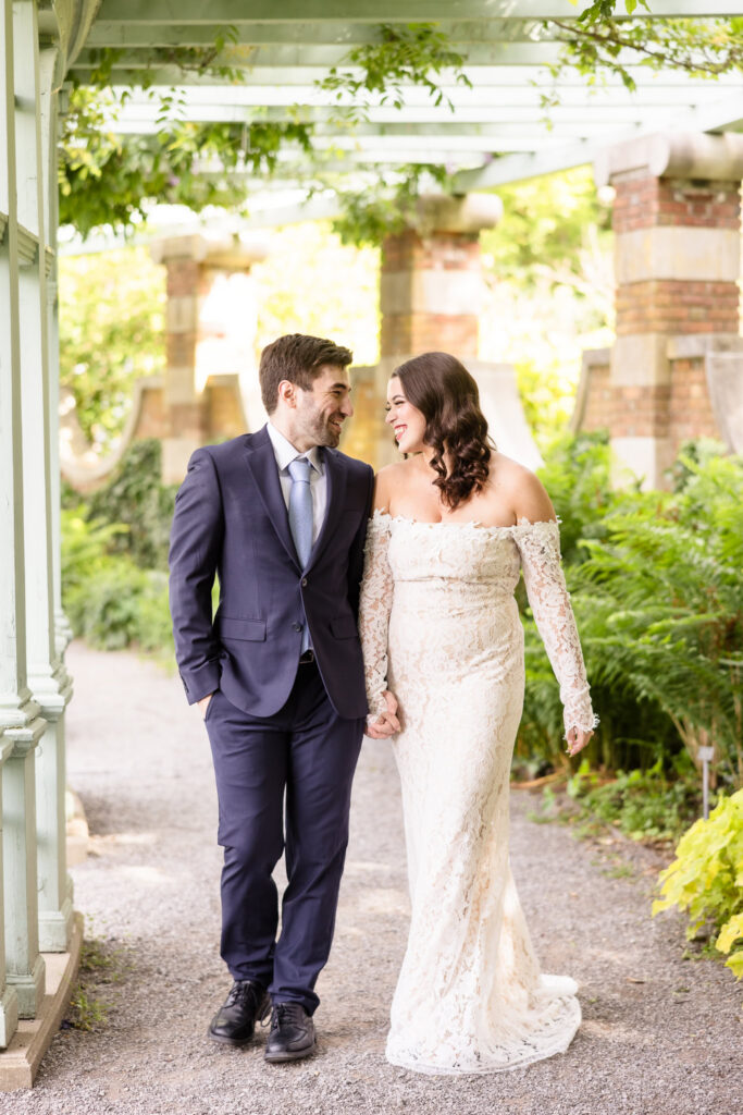 Couple walking hand in hand through a garden pathway during an editorial Old Westbury Gardens engagement session.