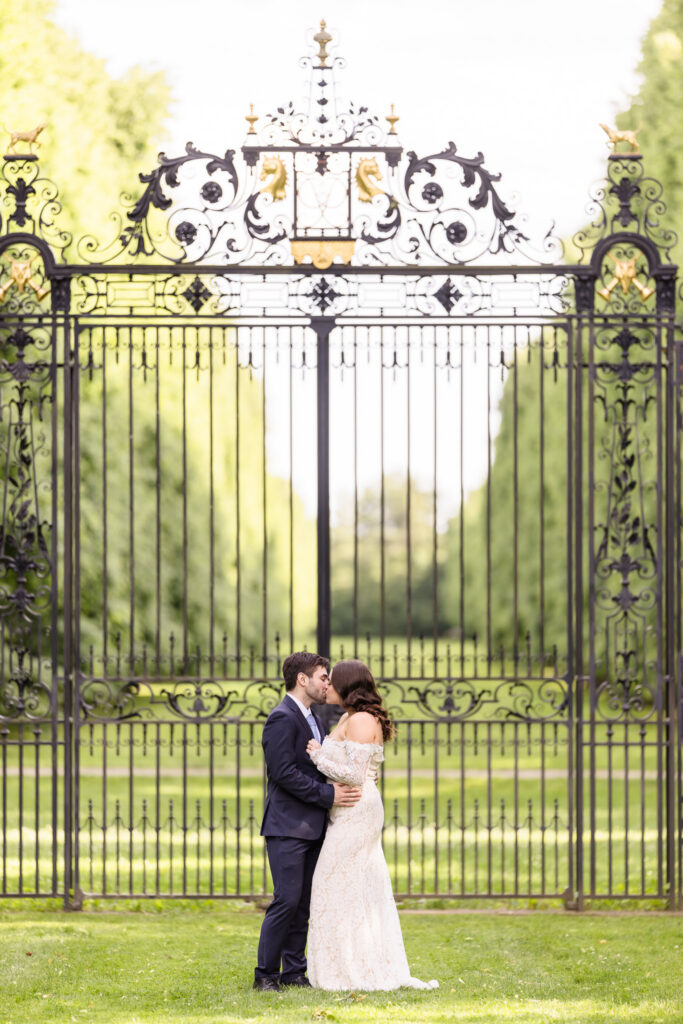 Couple sharing a kiss in front of the historic estate gates during an editorial Old Westbury Gardens engagement session.