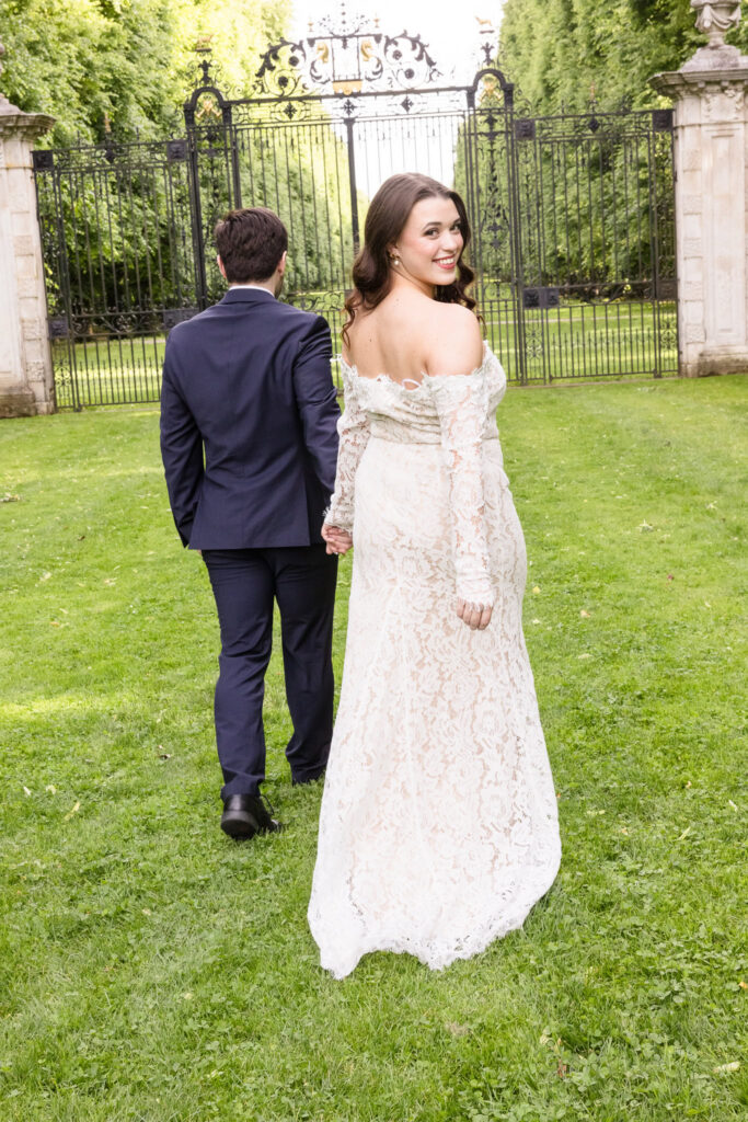 Bride smiling over her shoulder while leading her fiancé across the lawn.