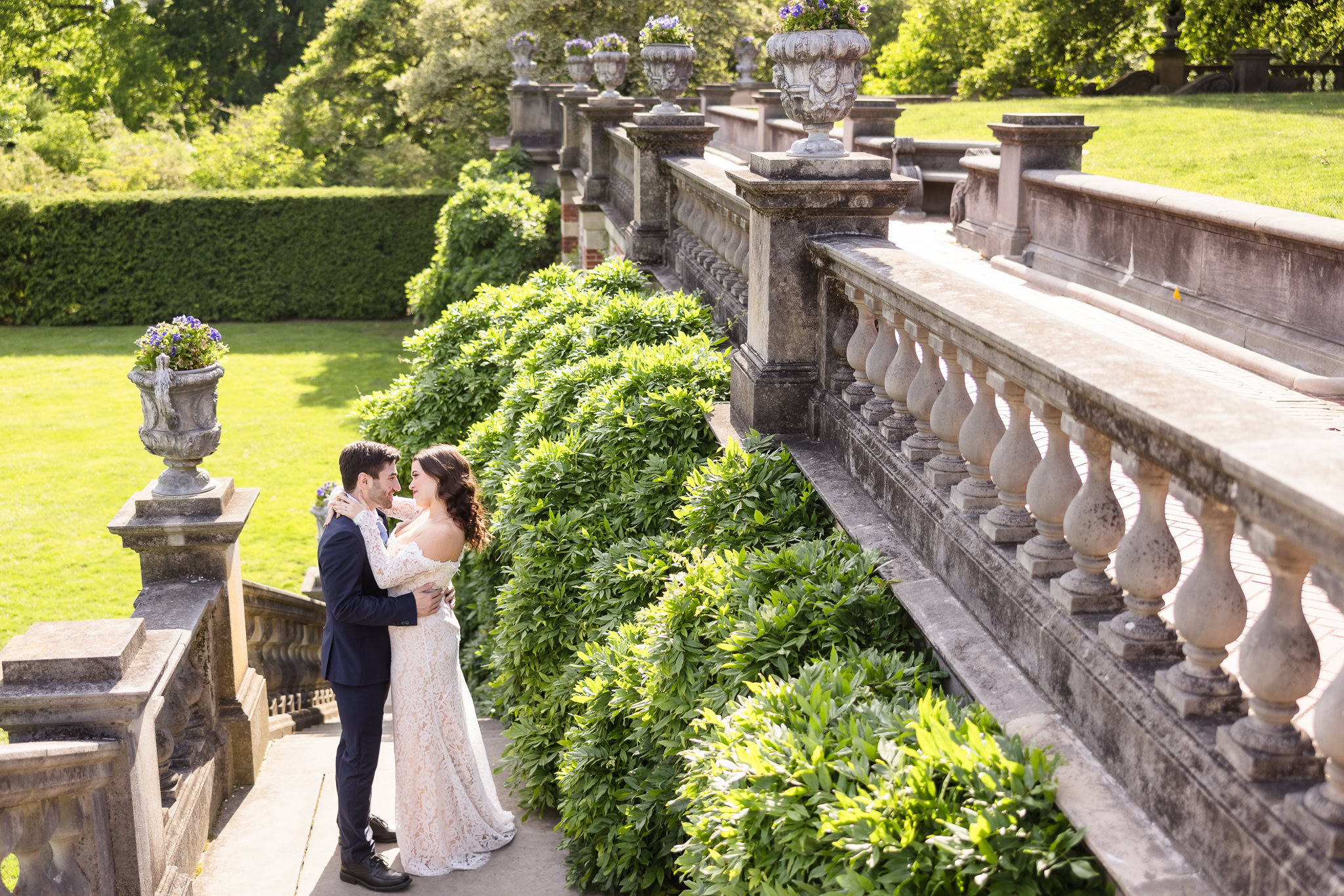 Couple embracing beside the stone balustrades and manicured hedges during an editorial Old Westbury Gardens engagement session.