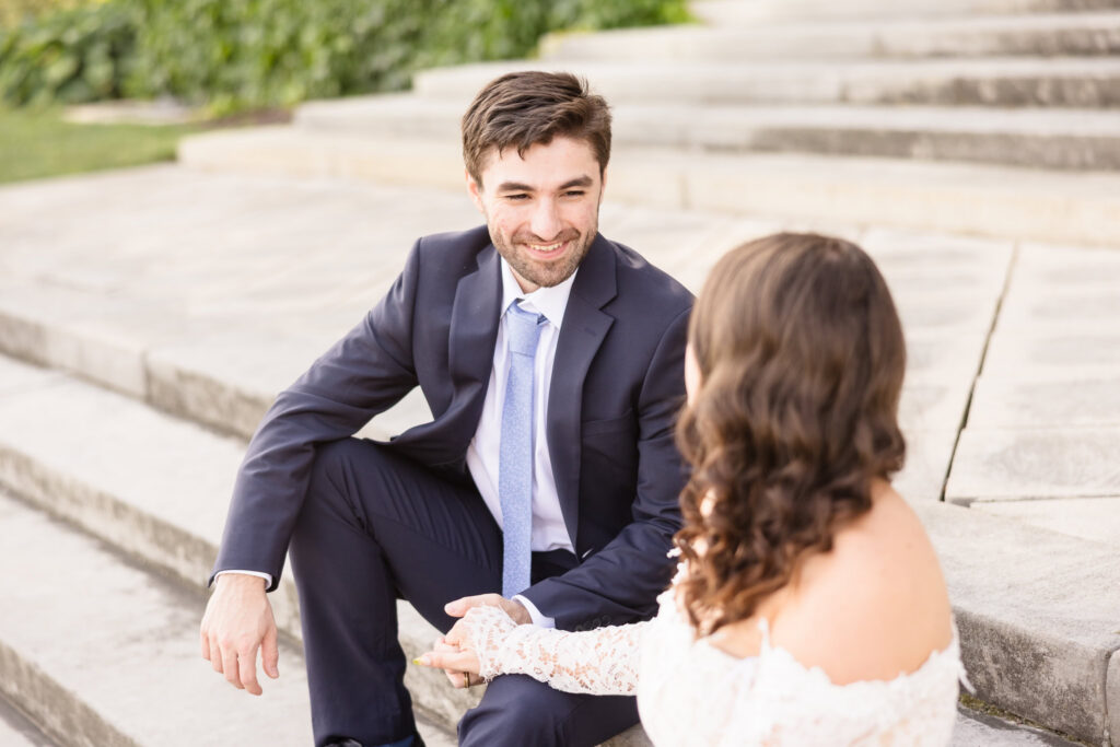 Groom smiling at his fiancée while seated on the mansion steps.