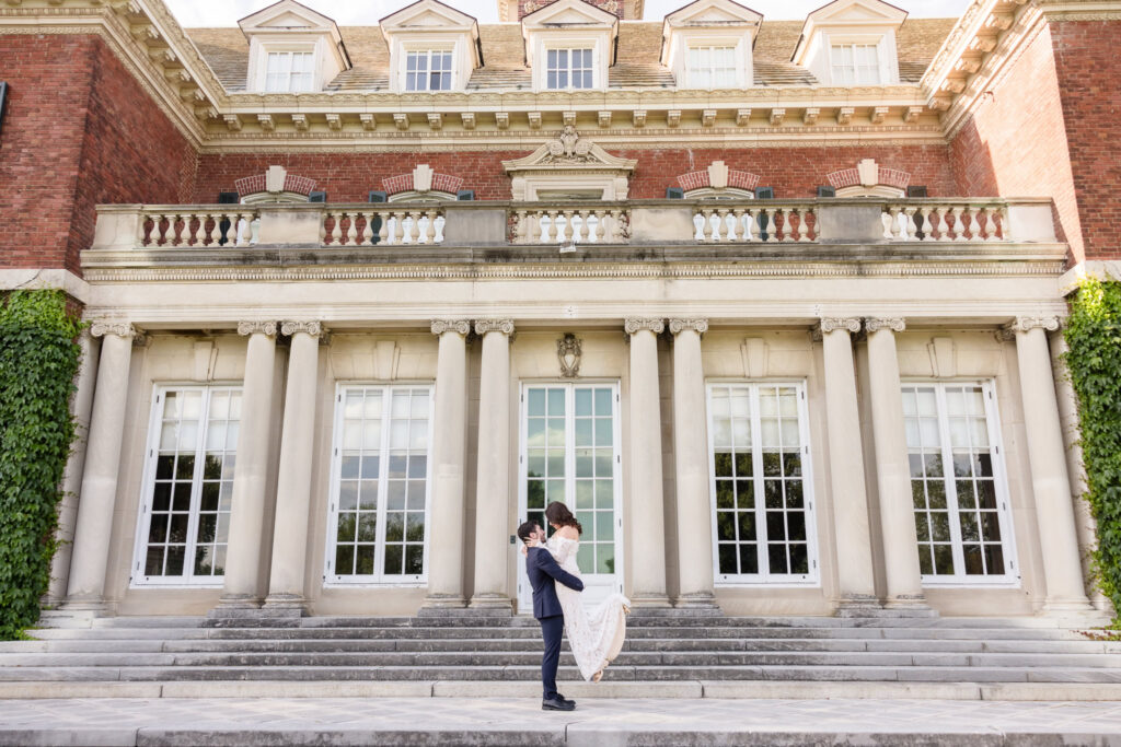 Wide editorial portrait of a couple framed by the grand columns of Westbury House during an Old Westbury Gardens engagement session.