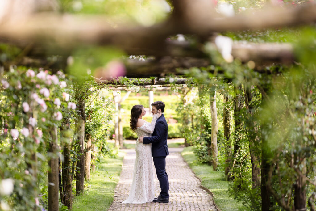 Couple embracing beneath a rose-covered pergola.