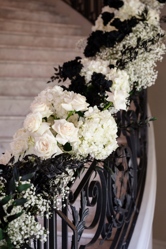 Close-up of a floral staircase installation at a Park Chateau Wedding featuring white blooms, black accents, and ornate iron railings.