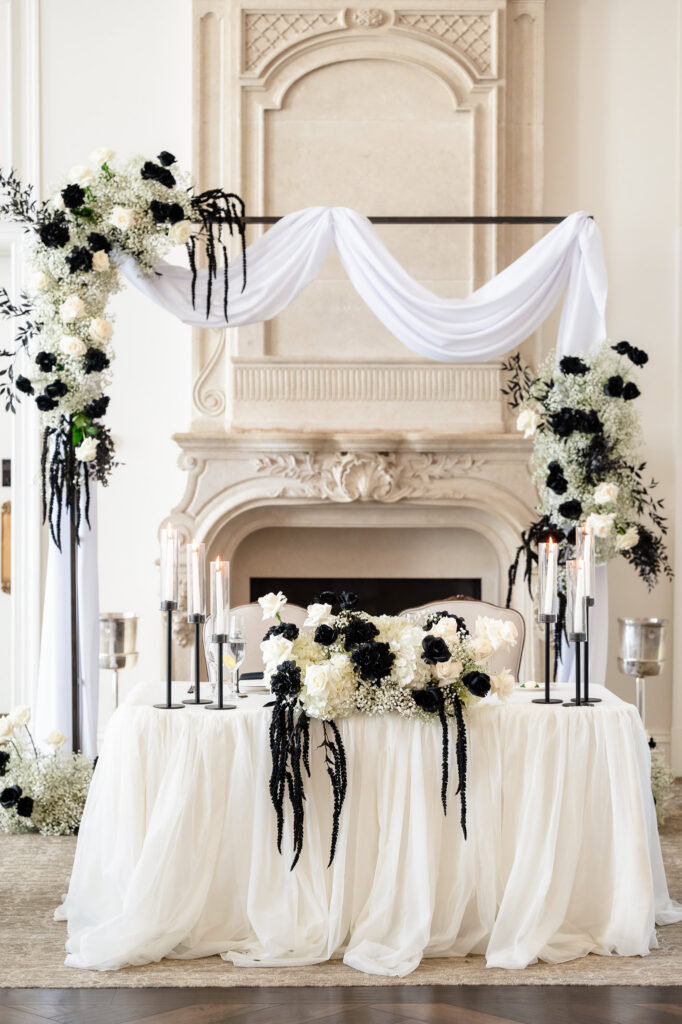 Sweetheart table design featuring dramatic black and white floral arrangements and candlelight.