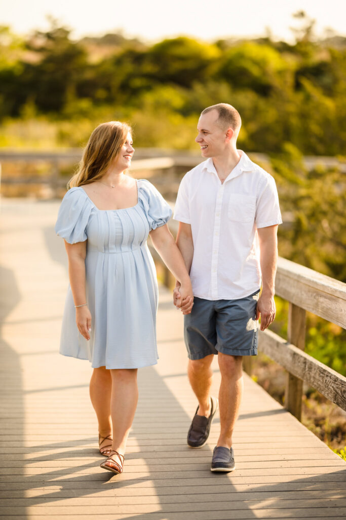 Couple walking hand in hand along the boardwalk near Robert Moses State Park during a sunlit engagement session.