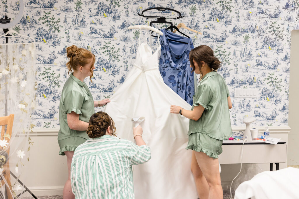 Bridesmaids steam Lydia's Suzanne Neville wedding dress while preparing for her June wedding at Briarcliff Manor.