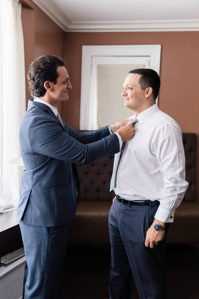 A groomsman helps Robbie straighten his tie while getting ready before the ceremony.