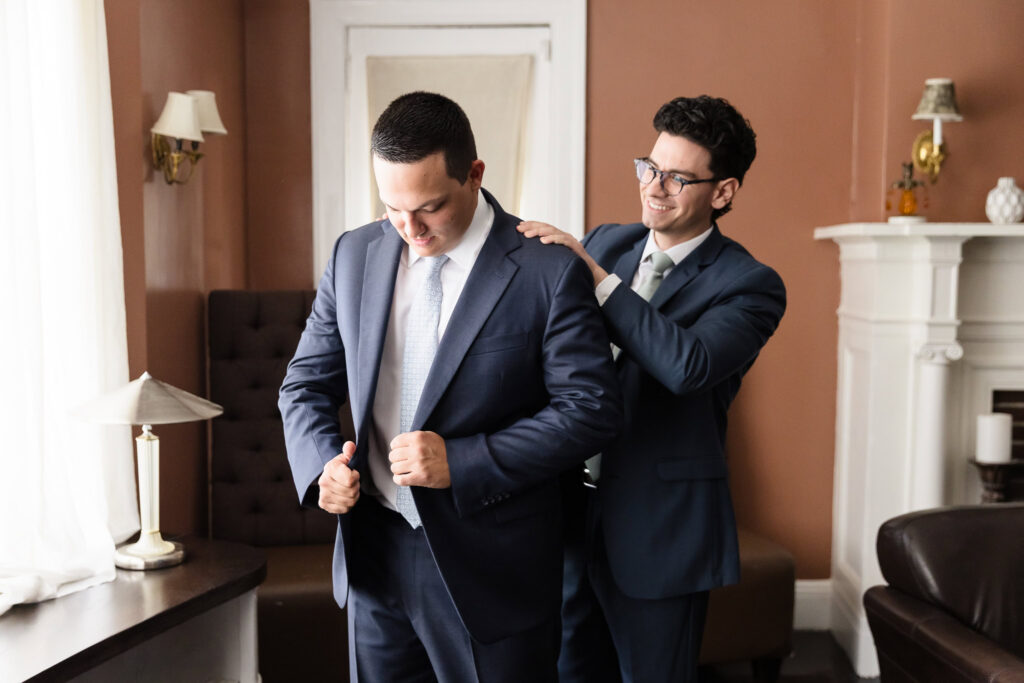 A groomsman helps Robbie put on his suit jacket during the morning preparations.