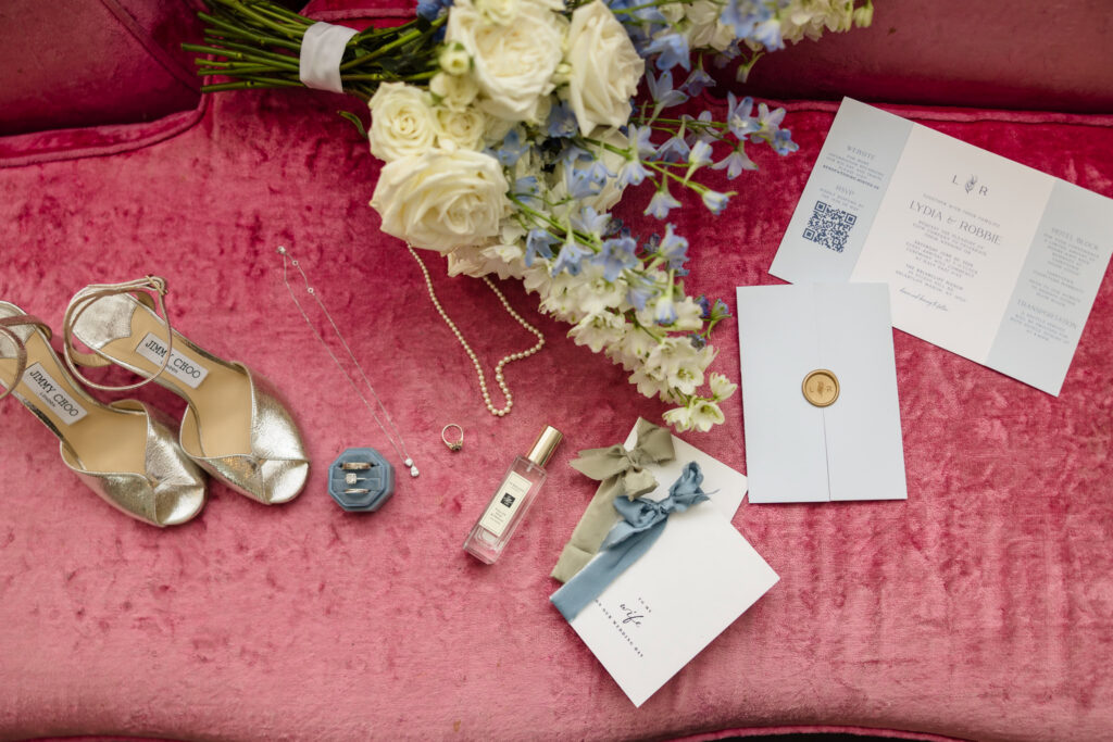 Lydia's bridal details including Jimmy Choo shoes, bouquet, wedding invitation suite, rings, jewelry, and perfume arranged together.