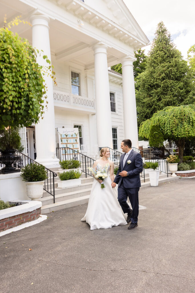 Lydia and Robbie walk hand in hand outside Briarcliff Manor during their wedding portraits.