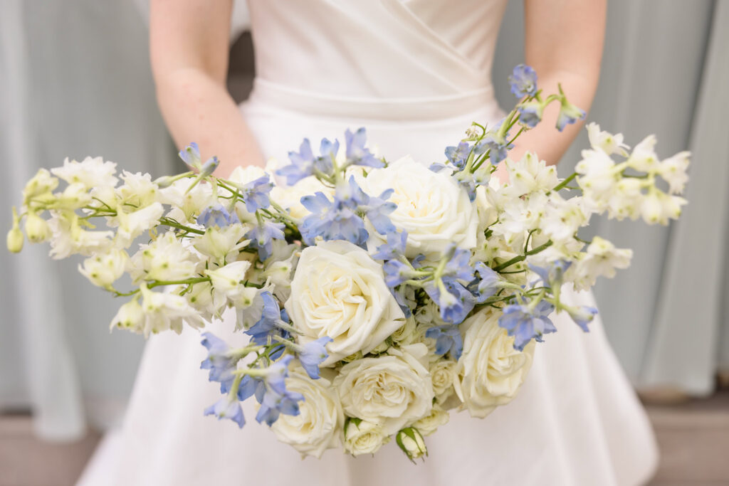 Close-up of Lydia's bridal bouquet featuring white roses, blue delphinium, and white florals during her Briarcliff Manor wedding.