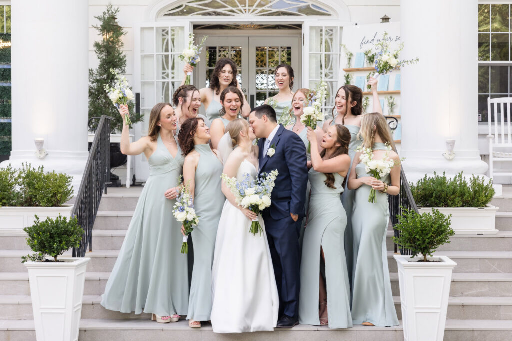 Bridesmaids celebrate around Lydia and Robbie as the newlyweds share a kiss outside Briarcliff Manor.