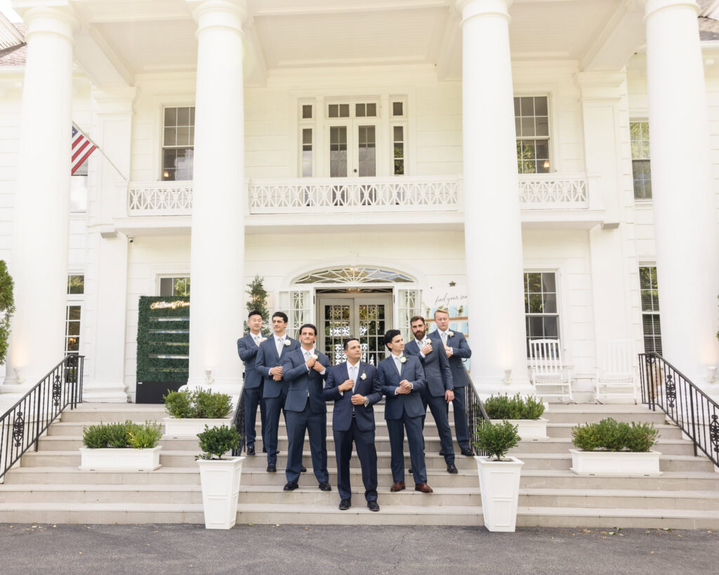 Groom and groomsmen pose confidently on the front steps beneath the iconic white columns of Briarcliff Manor.