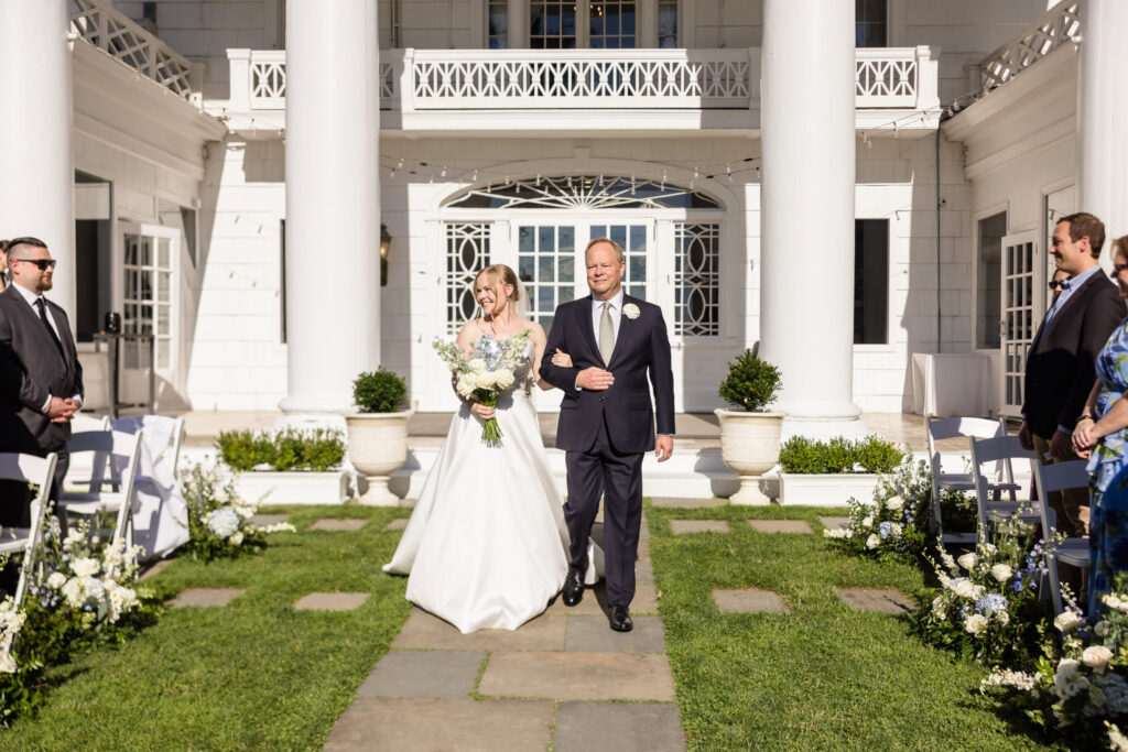 Lydia walks down the aisle with her father during her outdoor wedding ceremony at The Briarcliff Manor.