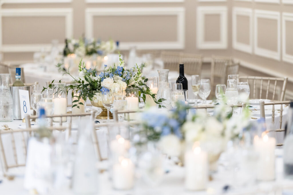 Reception tables decorated with blue and white floral centerpieces, candles, and elegant place settings at The Briarcliff Manor.