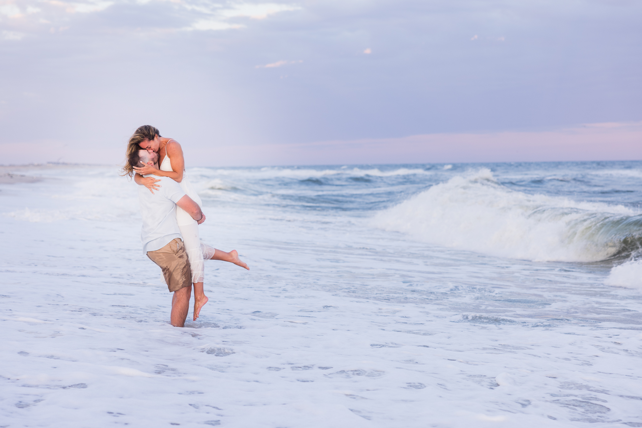 Couple embracing in the surf during sunset at Robert Moses State Park with dramatic waves and soft evening light.