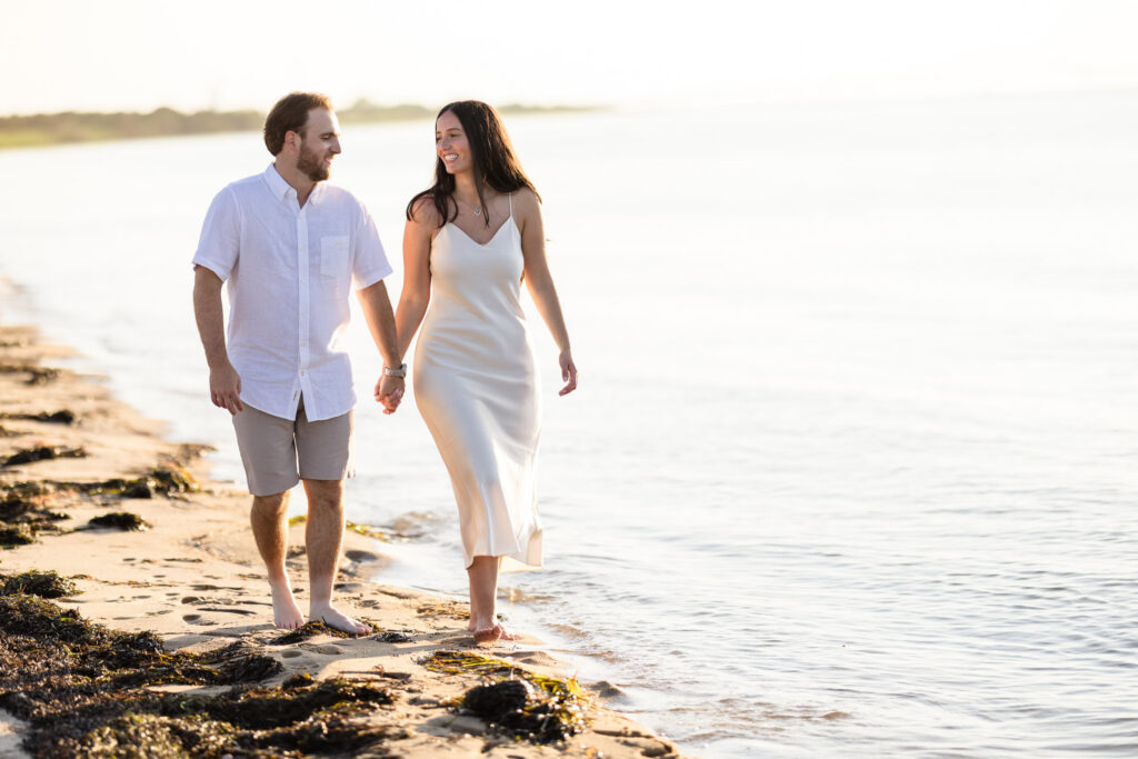 Catie and Zach walk hand in hand along the shoreline at Fire Island National Seashore during golden hour.