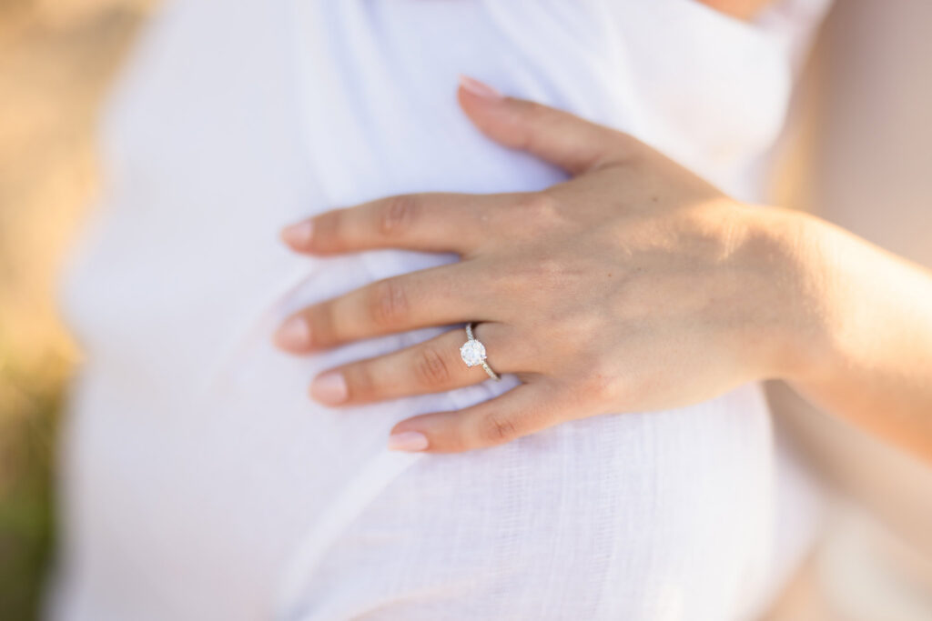 Close-up photograph of Catie's oval diamond engagement ring resting on Zach's shoulder during their engagement session.