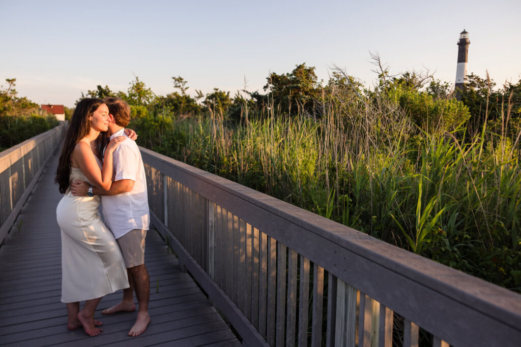 Catie and Zach embrace on the boardwalk near the Fire Island Lighthouse during golden hour at Fire Island National Seashore.