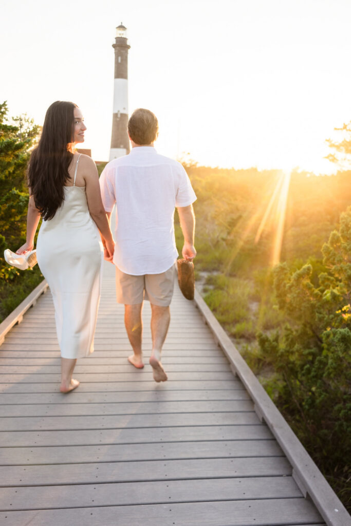 Catie and Zach walk hand in hand along the boardwalk toward the setting sun near Fire Island Lighthouse.