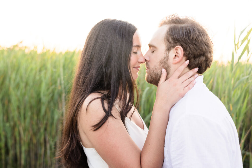 Catie gently holds Zach's face as they share a quiet moment surrounded by dune grass at Fire Island National Seashore.